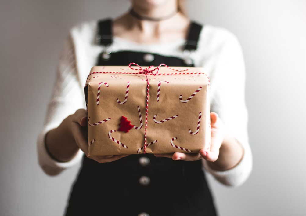 Image of a woman holding a gift in front of her with brown paper imprinted with candy canes plus red and white string